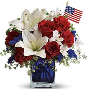 Bright red roses arranged amongst white Peruvian lilies and assorted greens. Accented with an American Flag. This stunning bouquet arrives arranged in a clear glass vase