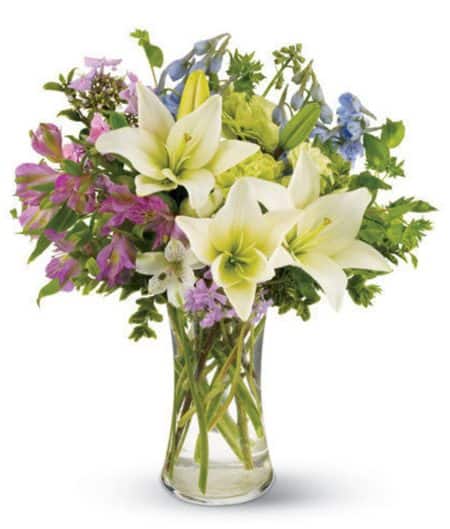 White lilies, blue delphinium and purple and green blossoms mingle together to create this casual bouque